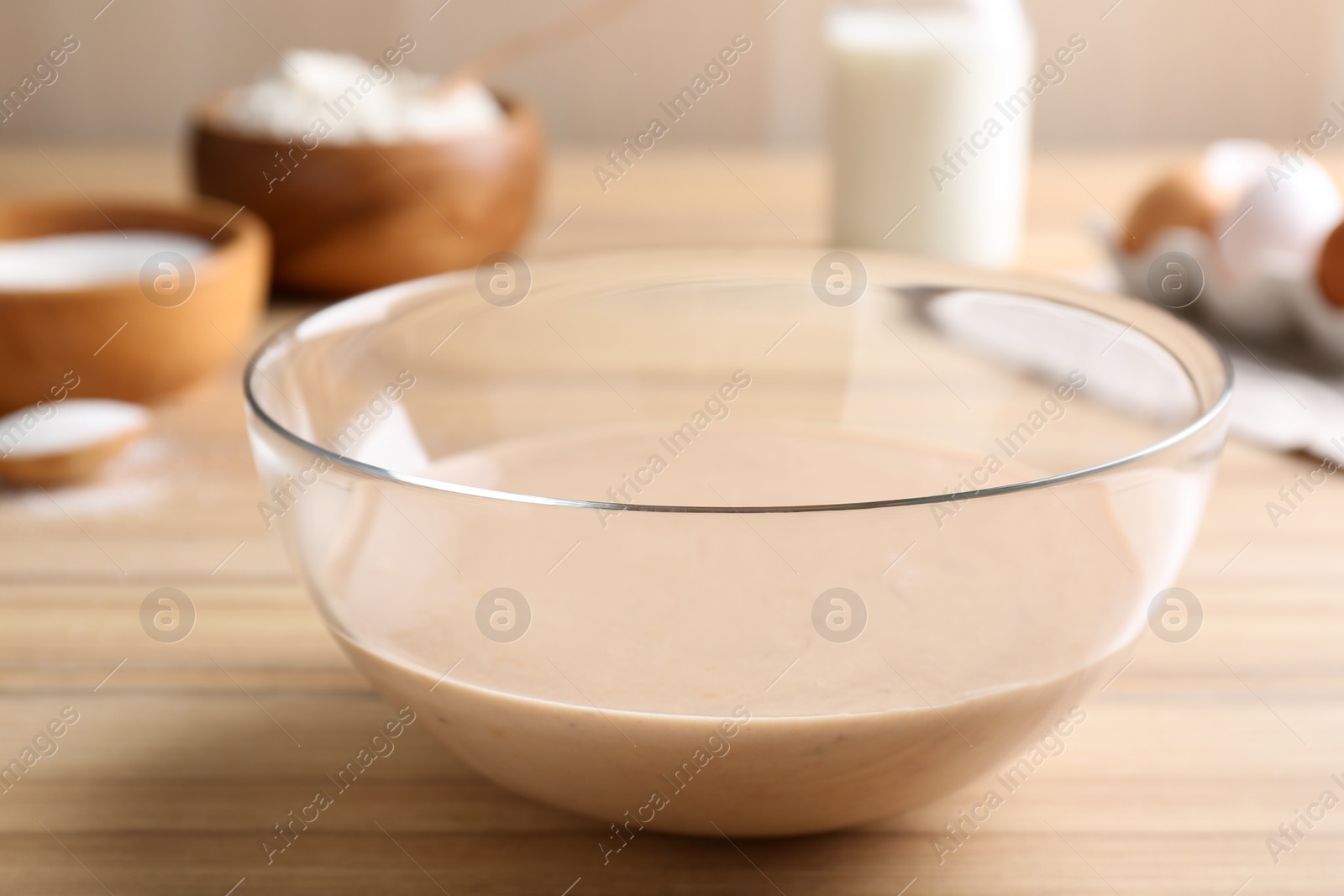 Photo of Glass bowl with batter on wooden table in kitchen, closeup