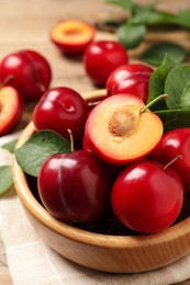 Delicious ripe cherry plums with leaves on wooden table, closeup