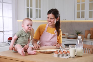 Photo of Happy young woman and her cute baby cooking together in kitchen, space for text