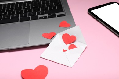 Photo of Long-distance relationship concept. Laptop, envelope with paper hearts and smartphone on pink background, closeup