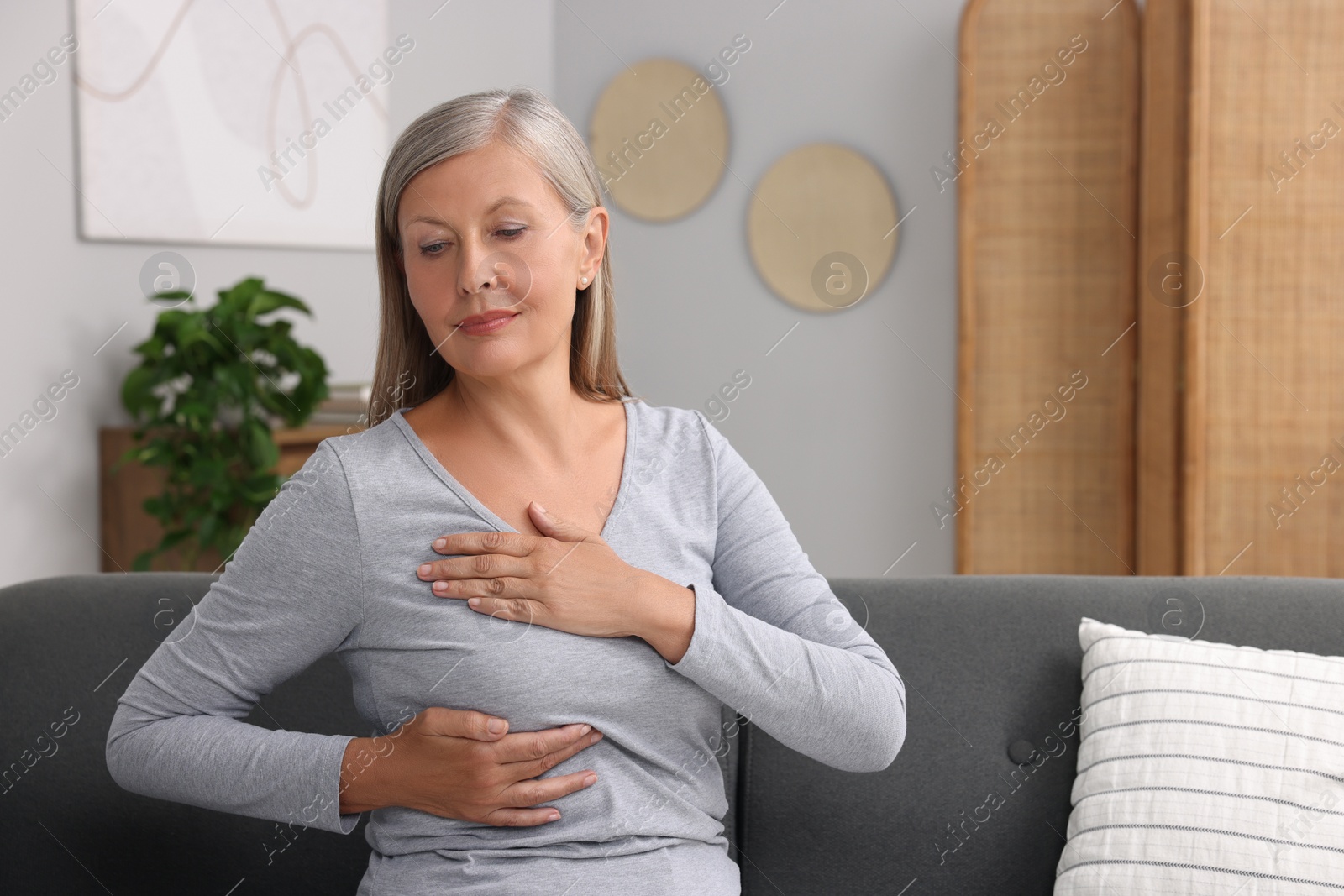 Photo of Beautiful senior woman doing breast self-examination at home, space for text