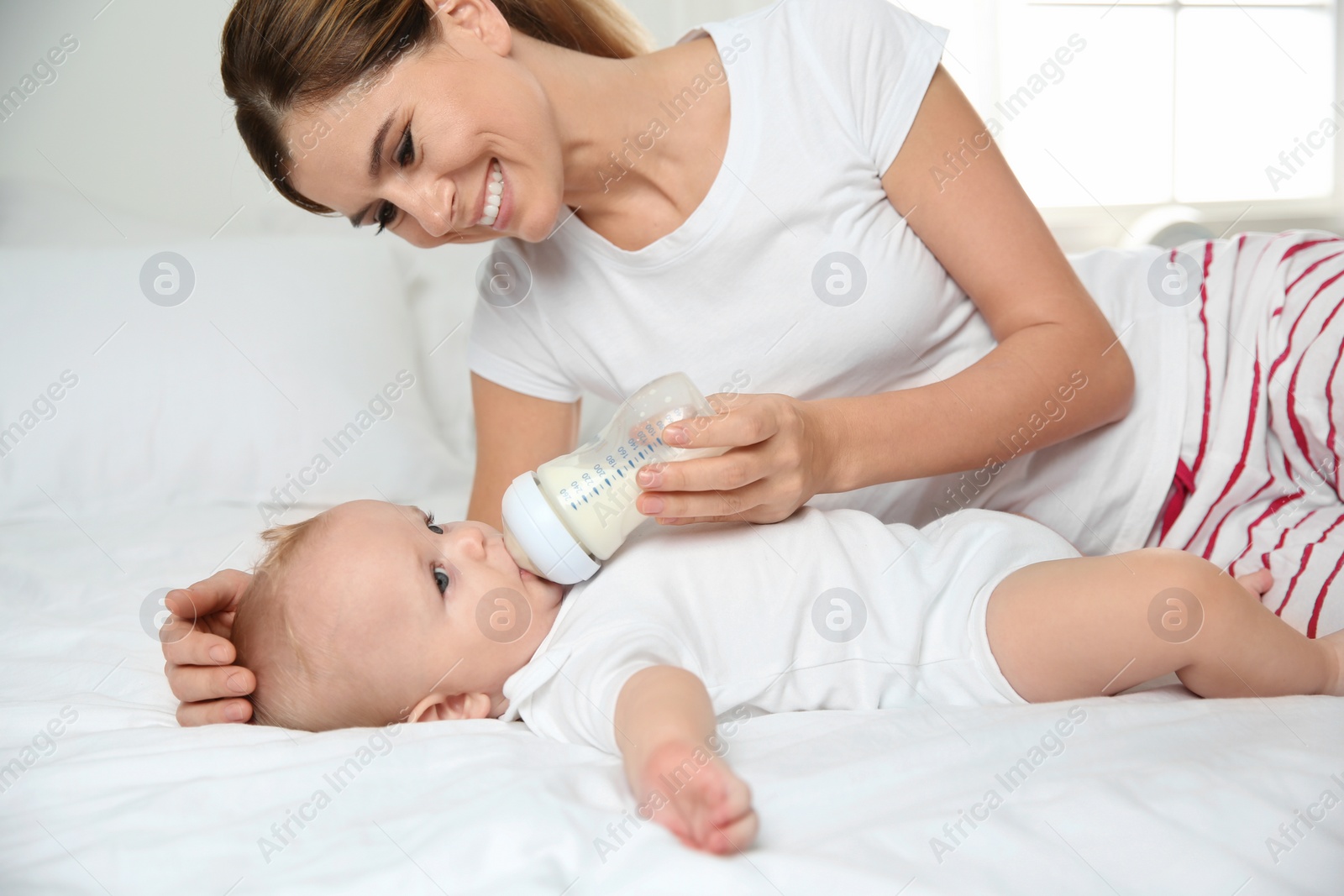 Photo of Lovely mother feeding her baby from bottle on bed at home