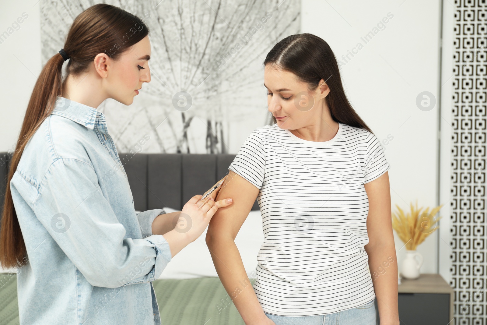 Photo of Woman giving insulin injection to her diabetic friend in bedroom