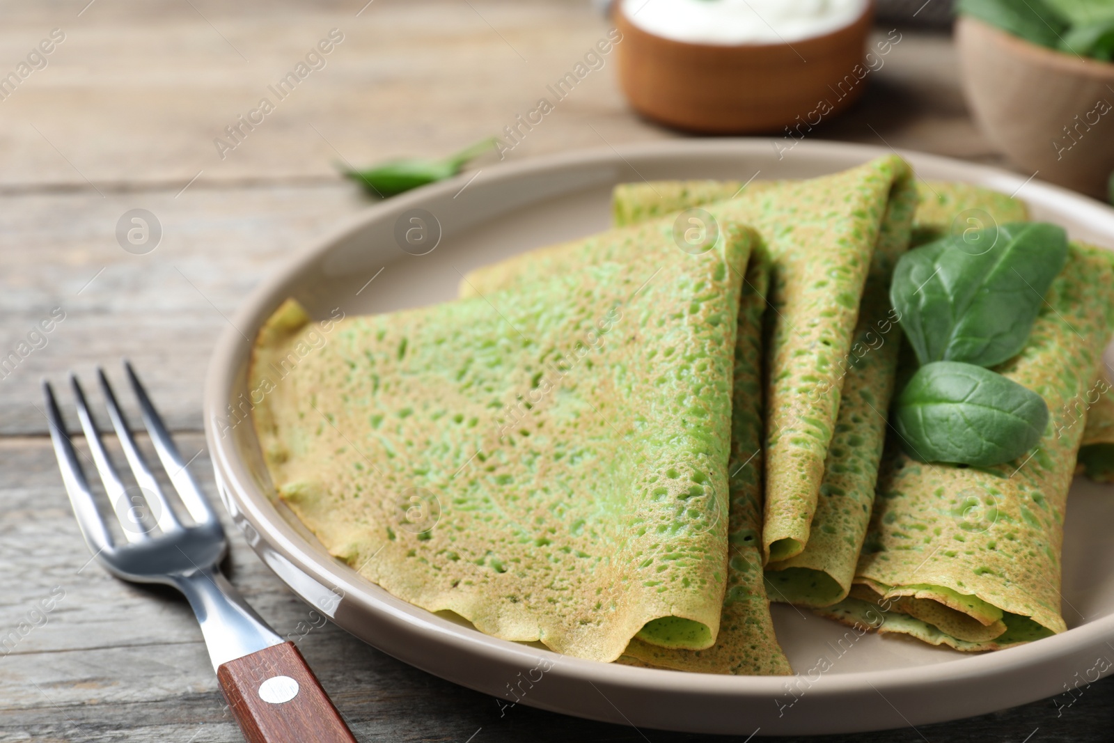 Photo of Delicious spinach crepes served on wooden table, closeup