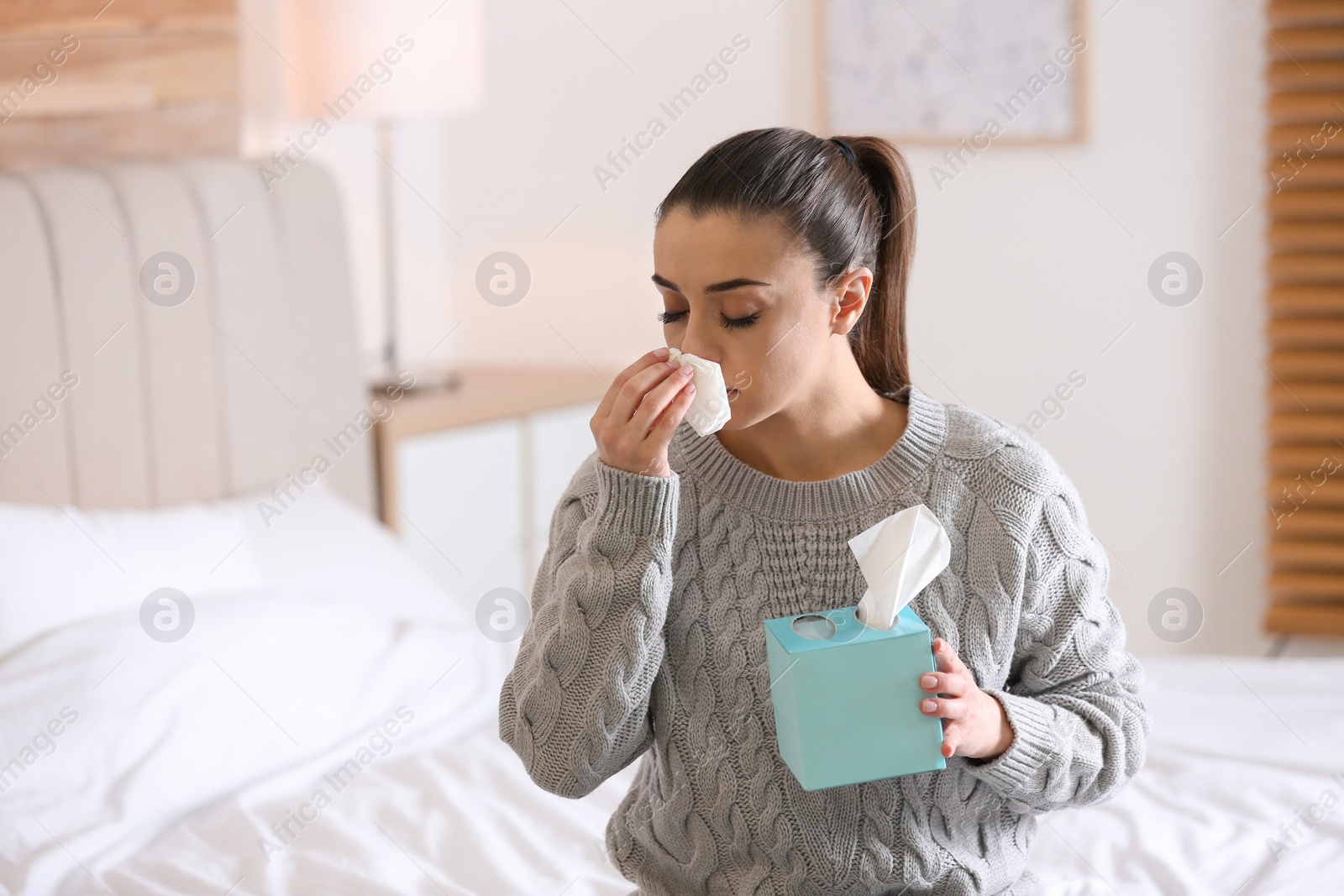 Photo of Ill woman with box of paper tissues on bed at home