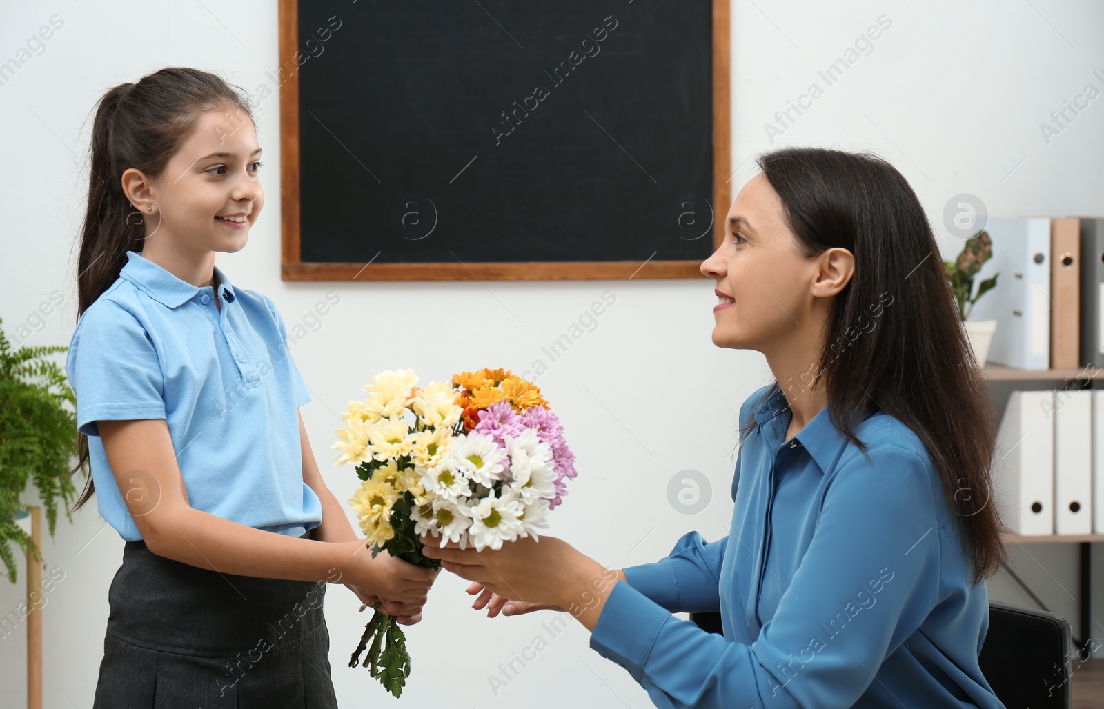 Photo of Schoolgirl congratulating her pedagogue with bouquet in classroom. Teacher's day