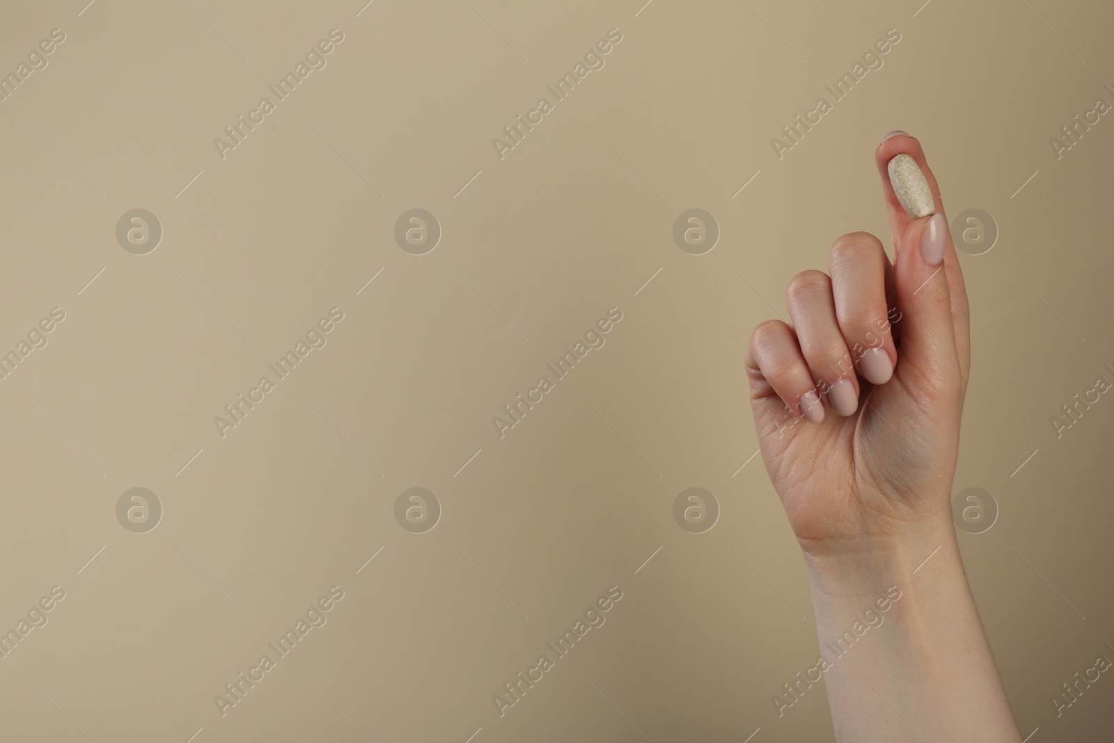 Photo of Woman holding vitamin pill on dark beige background, closeup with space for text. Health supplement