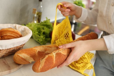 Photo of Woman taking baguette out from string bag at countertop, closeup