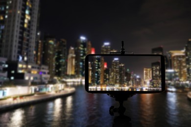 Image of DUBAI, UNITED ARAB EMIRATES - NOVEMBER 03, 2018: Night cityscape of marina district, blurred view. Taking photo with smartphone mounted on tripod