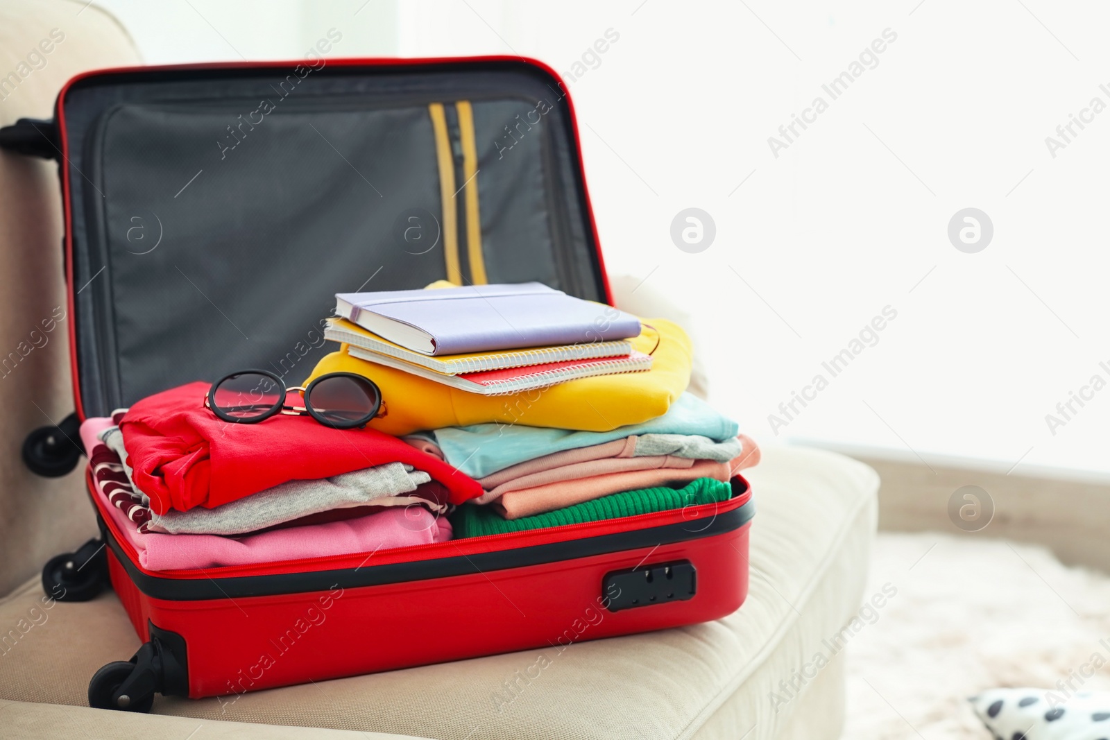 Photo of Travel suitcase with clothes and notebooks on sofa