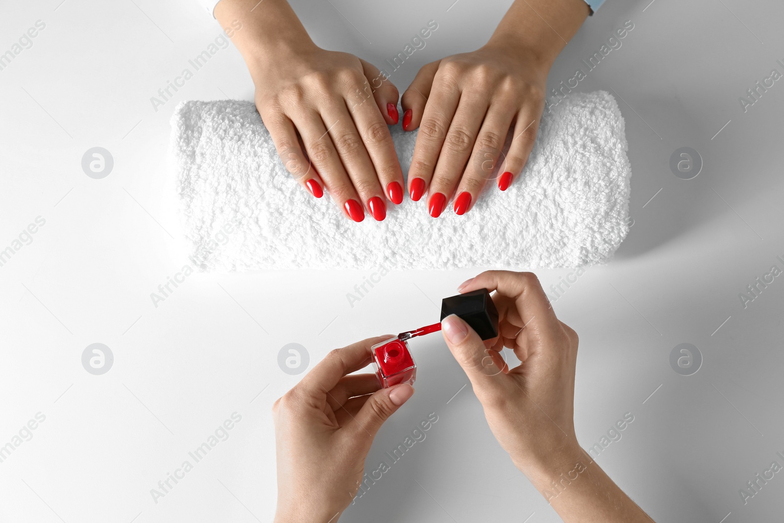 Photo of Manicurist painting client's nails with bright polish on white background, top view