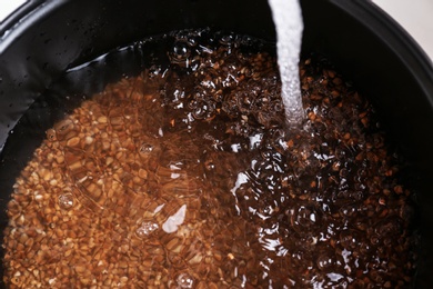 Photo of Pouring water into multi cooker with buckwheat, closeup