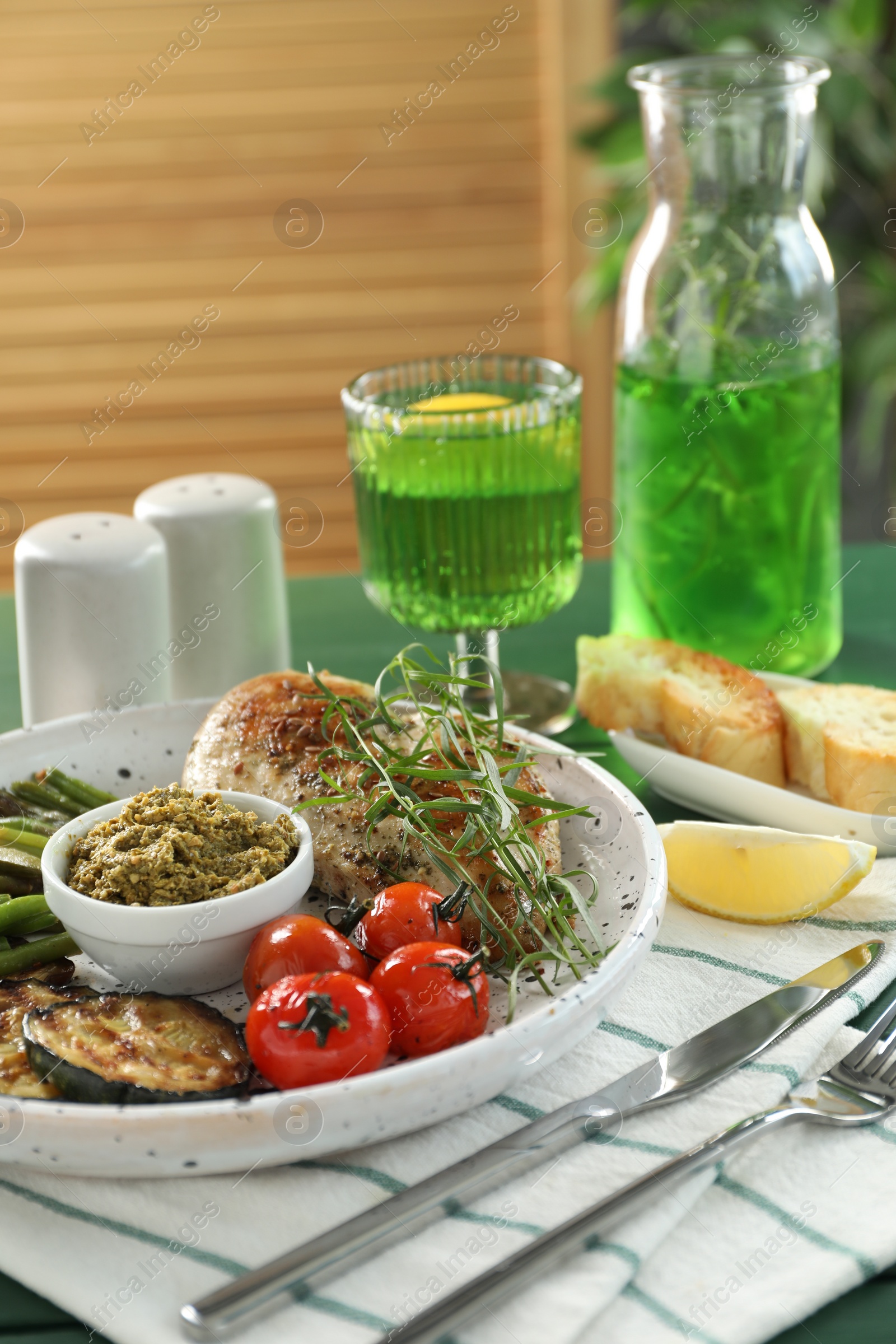 Photo of Tasty chicken, vegetables with tarragon and pesto sauce served on green table
