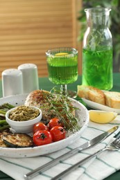 Photo of Tasty chicken, vegetables with tarragon and pesto sauce served on green table