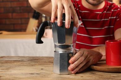 Photo of Brewing coffee. Man with moka pot at wooden table indoors, closeup. Space for text