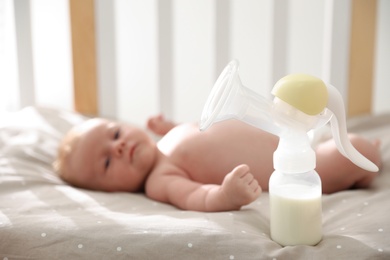 Photo of Healthy baby lying in cot, focus on breast pump with milk