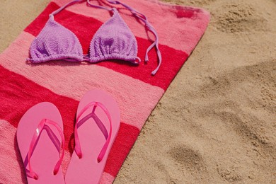 Photo of Beach towel with slippers and swimsuit on sand, space for text