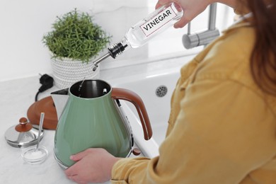 Photo of Woman pouring vinegar from bottle into electric kettle in kitchen, closeup