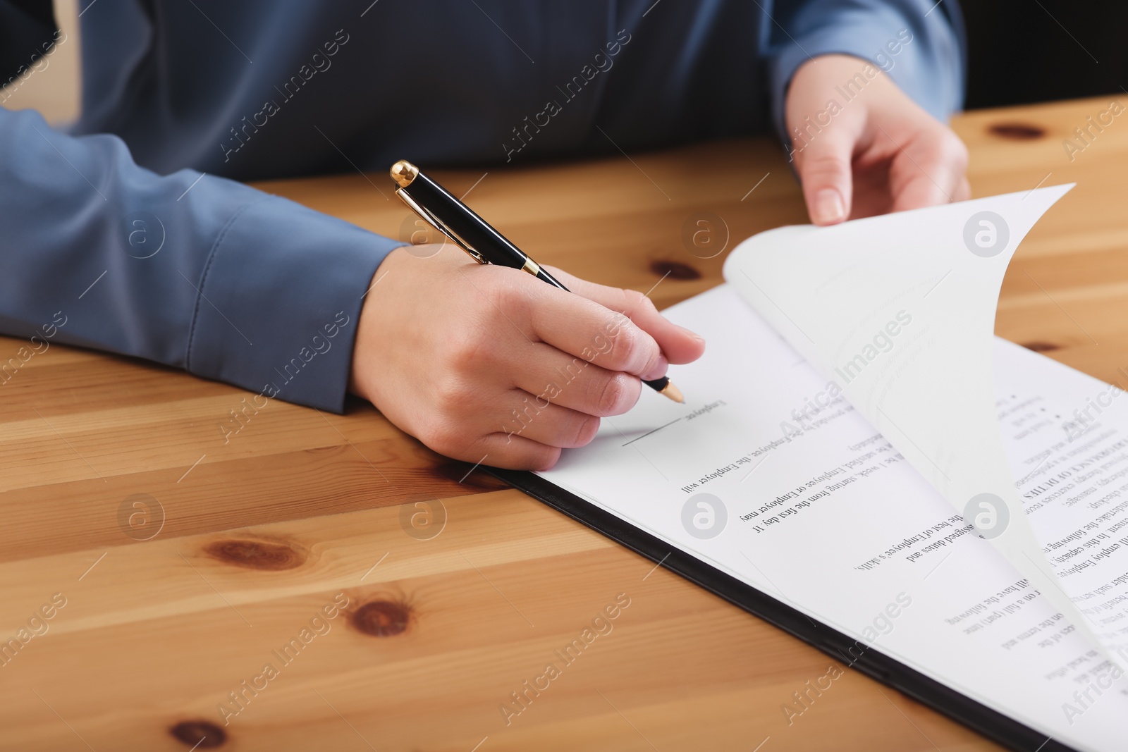 Photo of Businesswoman signing contract at wooden table, closeup of hands