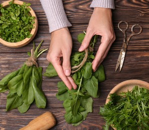 Photo of Woman with fresh green herbs at wooden table, top view