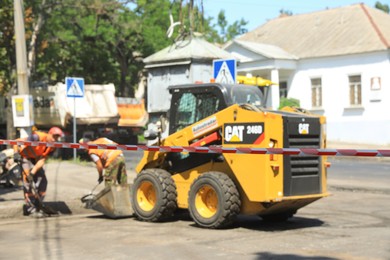Photo of MYKOLAIV, UKRAINE - AUGUST 04, 2021: Workers with road repair machinery laying new asphalt, focus on construction tape