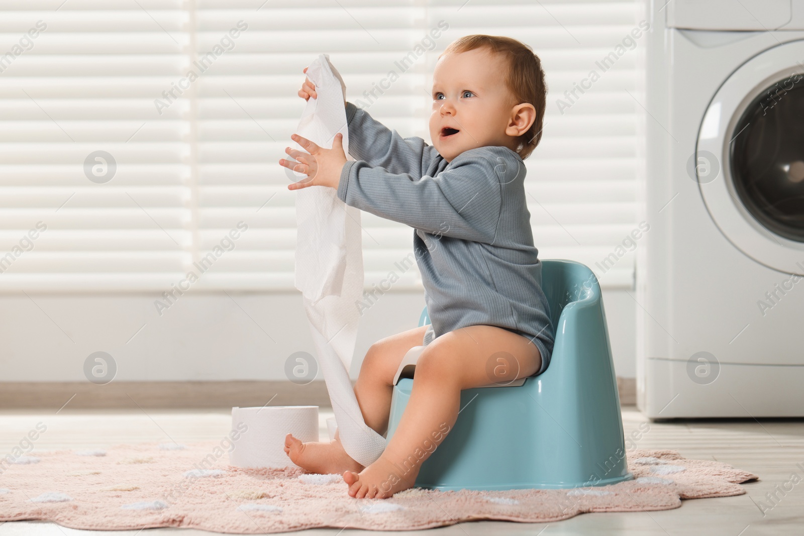 Photo of Little child with toilet paper roll sitting on plastic baby potty indoors. Space for text