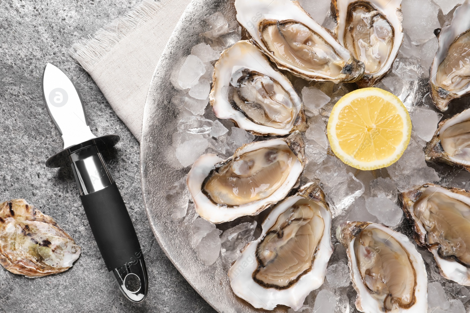 Photo of Delicious fresh oysters with lemon served on grey table, flat lay