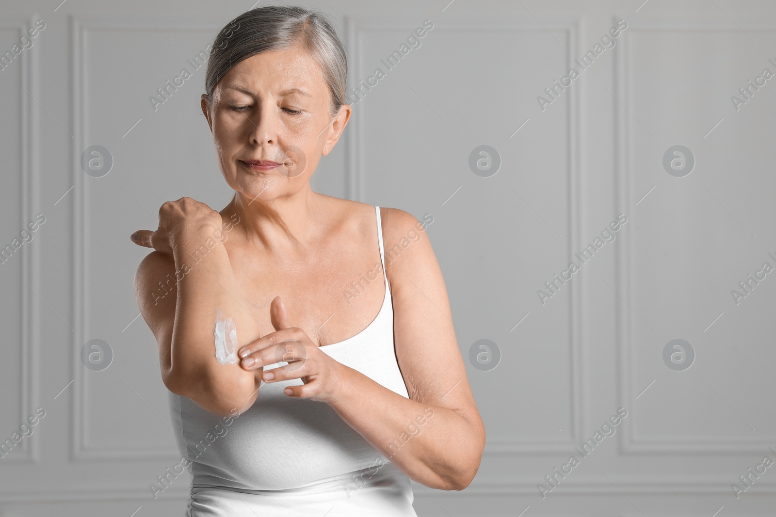 Photo of Woman applying body cream onto elbow near white wall. Space for text