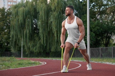 Photo of Muscular man doing exercise with elastic resistance band at stadium