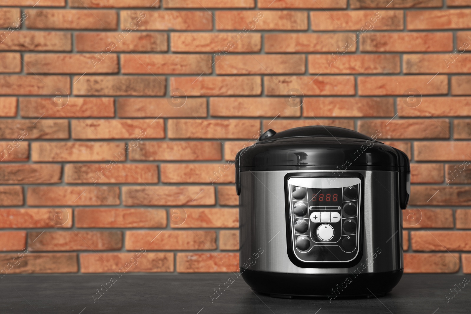 Photo of Modern electric multi cooker on table near brick wall. Space for text