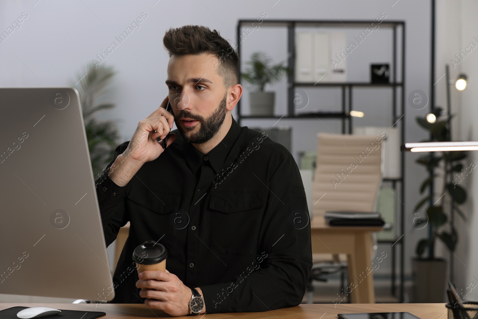 Photo of Man talking on phone while working at table in office