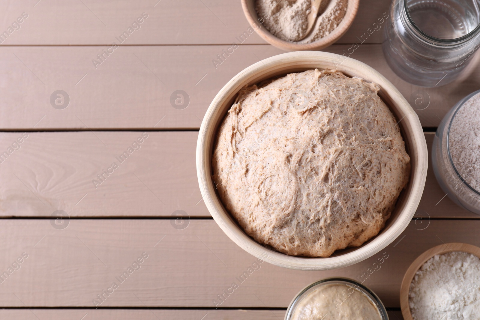Photo of Fresh sourdough, flour and water on wooden table, flat lay. Space for text