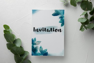 Photo of Beautiful card with word Invitation and eucalyptus leaves on white table, flat lay