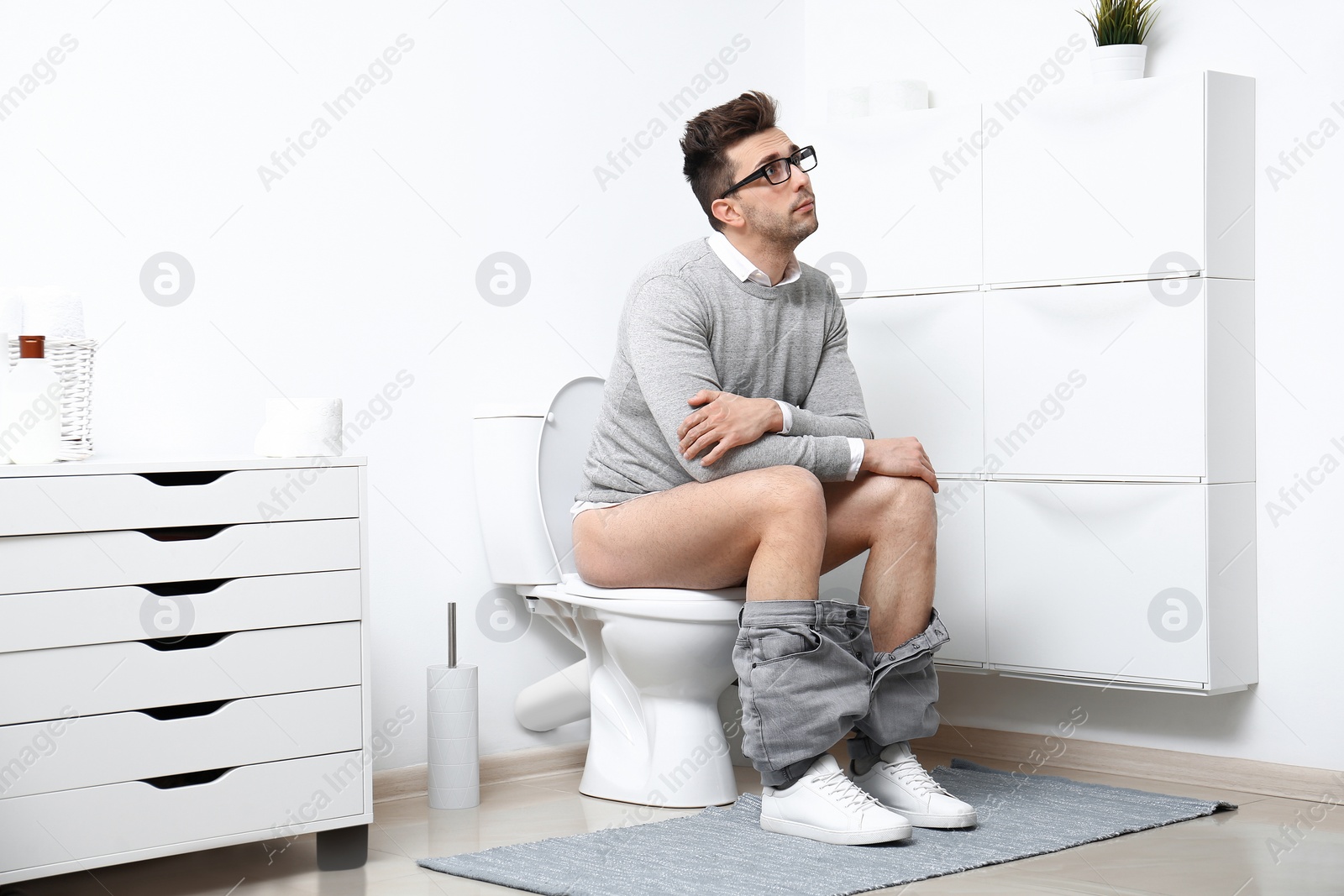 Photo of Man with glasses sitting on toilet bowl in bathroom