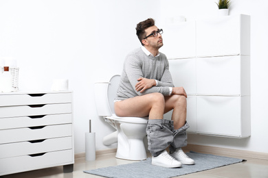 Man with glasses sitting on toilet bowl in bathroom