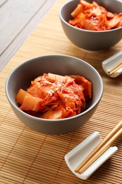 Bowls of spicy cabbage kimchi and chopsticks on bamboo mat