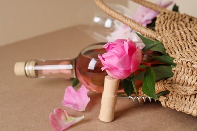 Photo of Corkscrew near wicker bag with bottle of rose wine and beautiful pink peonies on brown background, closeup