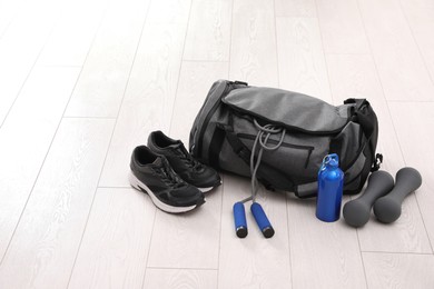 Photo of Sports bag and gym equipment on white floor. Space for text