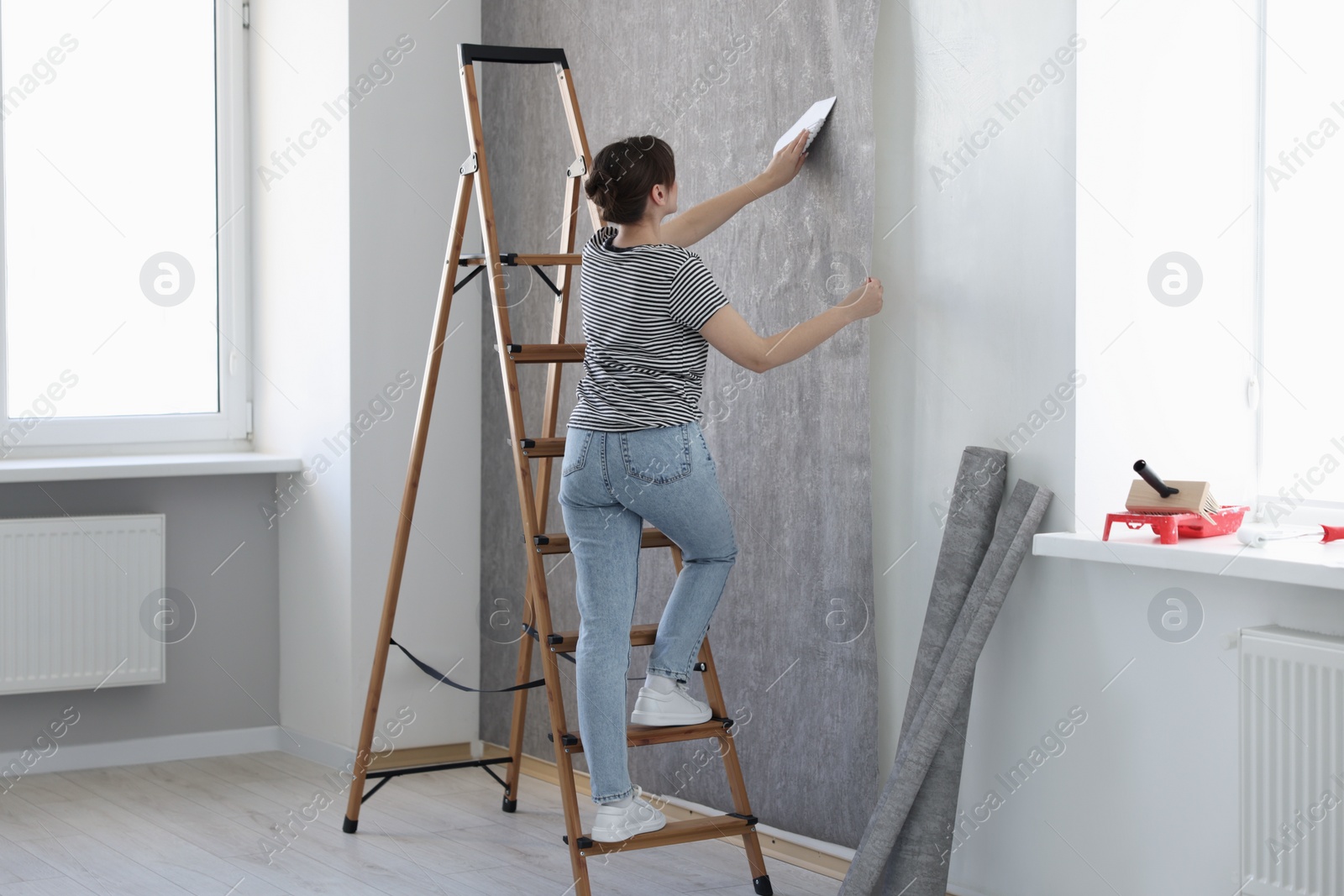 Photo of Woman smoothing stylish gray wallpaper in room