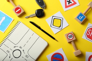 Photo of Flat lay composition with workbook for driving lessons and road signs on yellow background. Passing license exam
