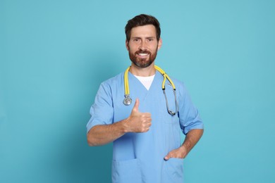 Photo of Doctor with stethoscope showing thumb up on light blue background