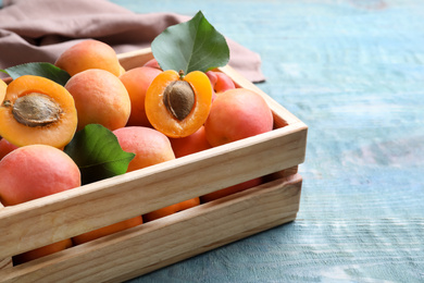 Photo of Delicious fresh ripe apricots in crate on blue wooden table, closeup