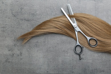 Photo of Flat lay composition with light brown hair and thinning scissors on grey background. Hairdresser service