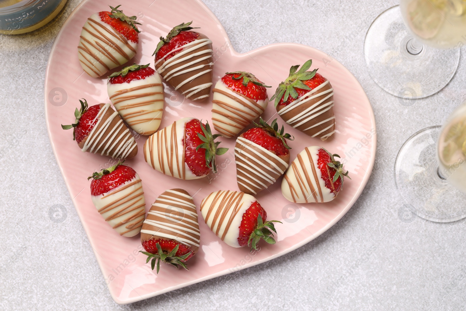 Photo of Heart shaped plate with delicious chocolate covered strawberries and sparkling wine on light table, flat lay