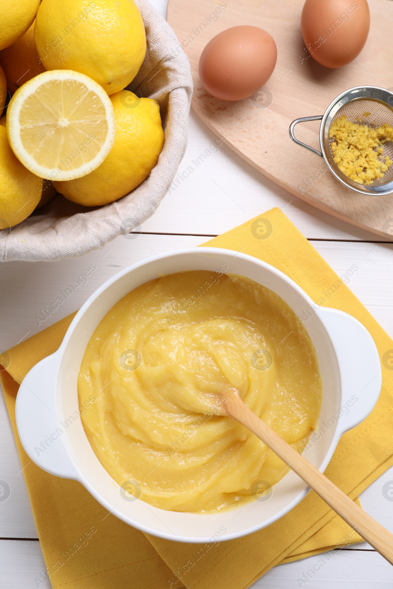 Photo of Delicious lemon curd in bowl, ingredients, spoon and sieve on white wooden table, flat lay