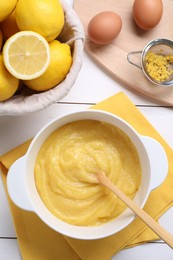 Photo of Delicious lemon curd in bowl, ingredients, spoon and sieve on white wooden table, flat lay