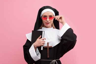 Photo of Woman in nun habit and sunglasses holding Bible against pink background. Sexy costume