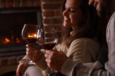 Lovely couple with glasses of wine near fireplace at home, closeup. Winter vacation