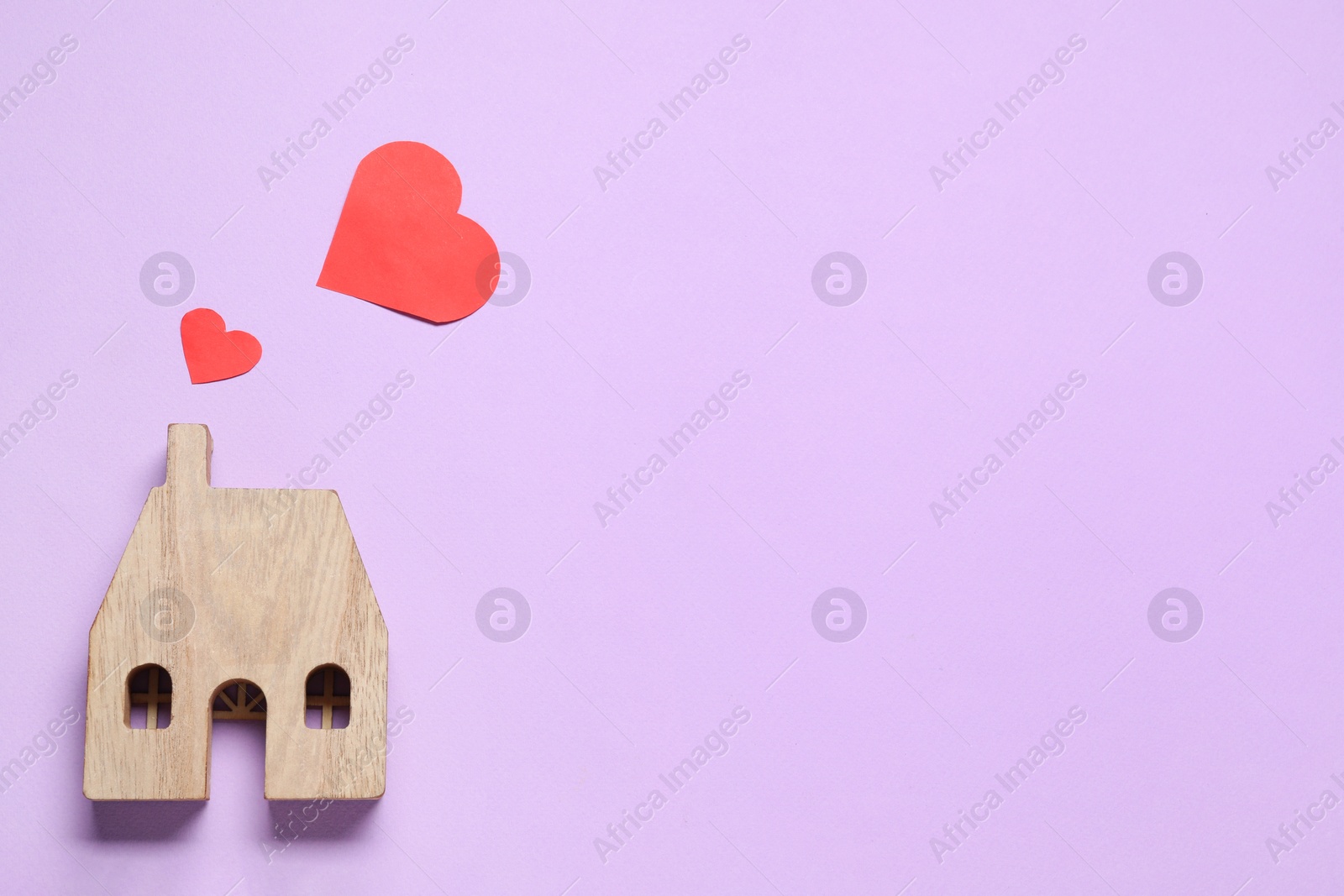 Photo of Long-distance relationship concept. Wooden house model and decorative hearts on violet background, flat lay with space for text