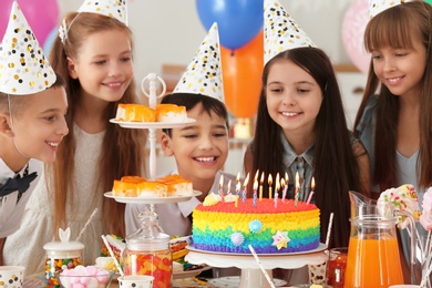 Happy children near cake with candles at birthday party indoors